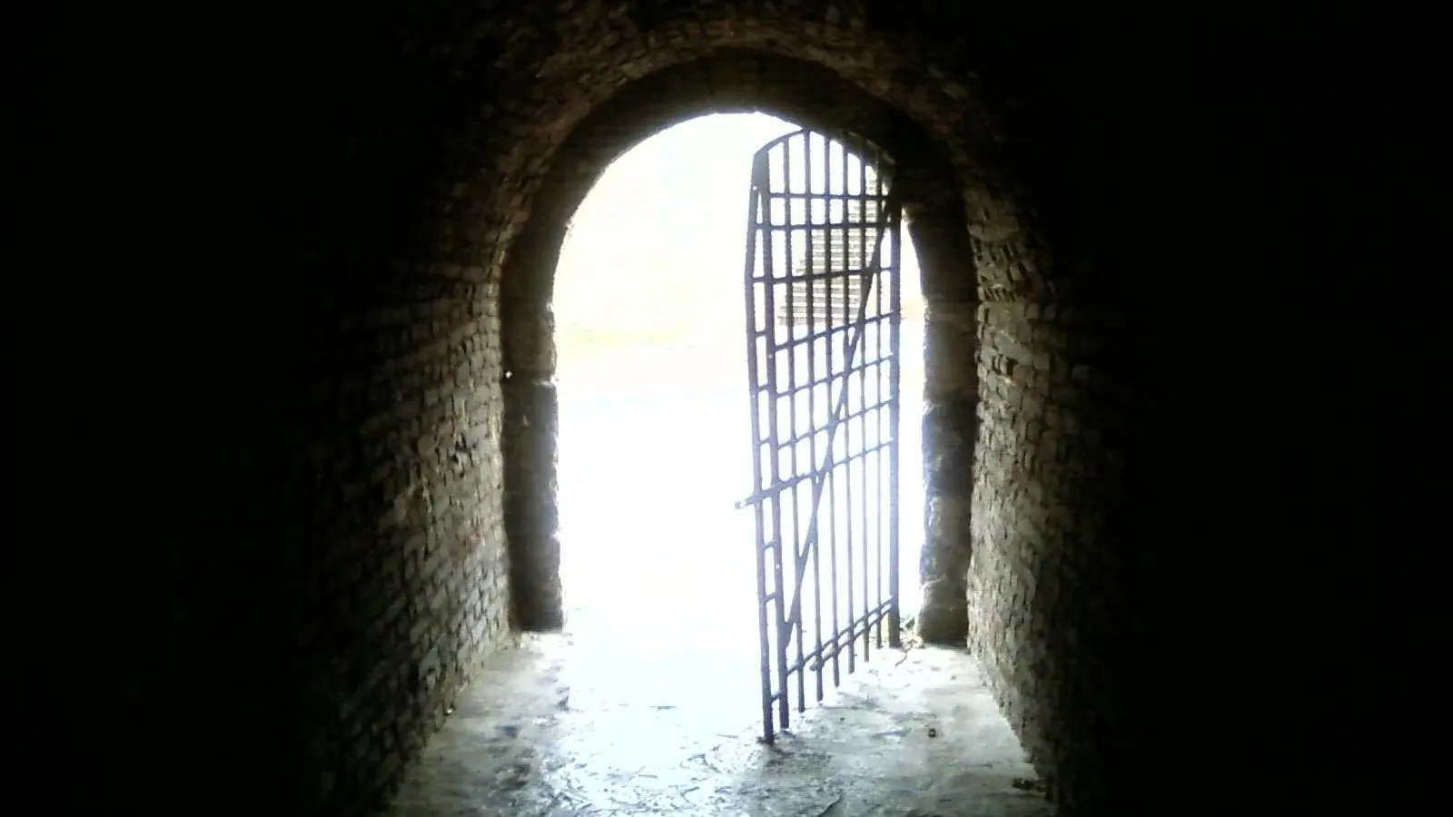 Grille ouverte au bout d'un passage voûté, baignée de lumière