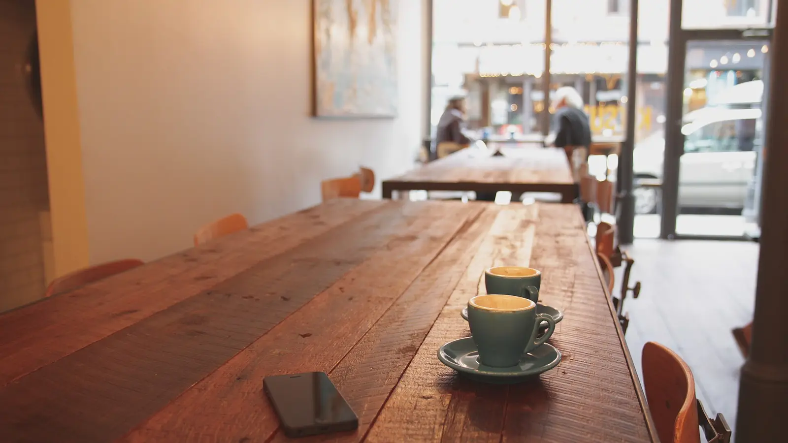 Une tasse de café et un téléphone posés sur la table en bois d'un café