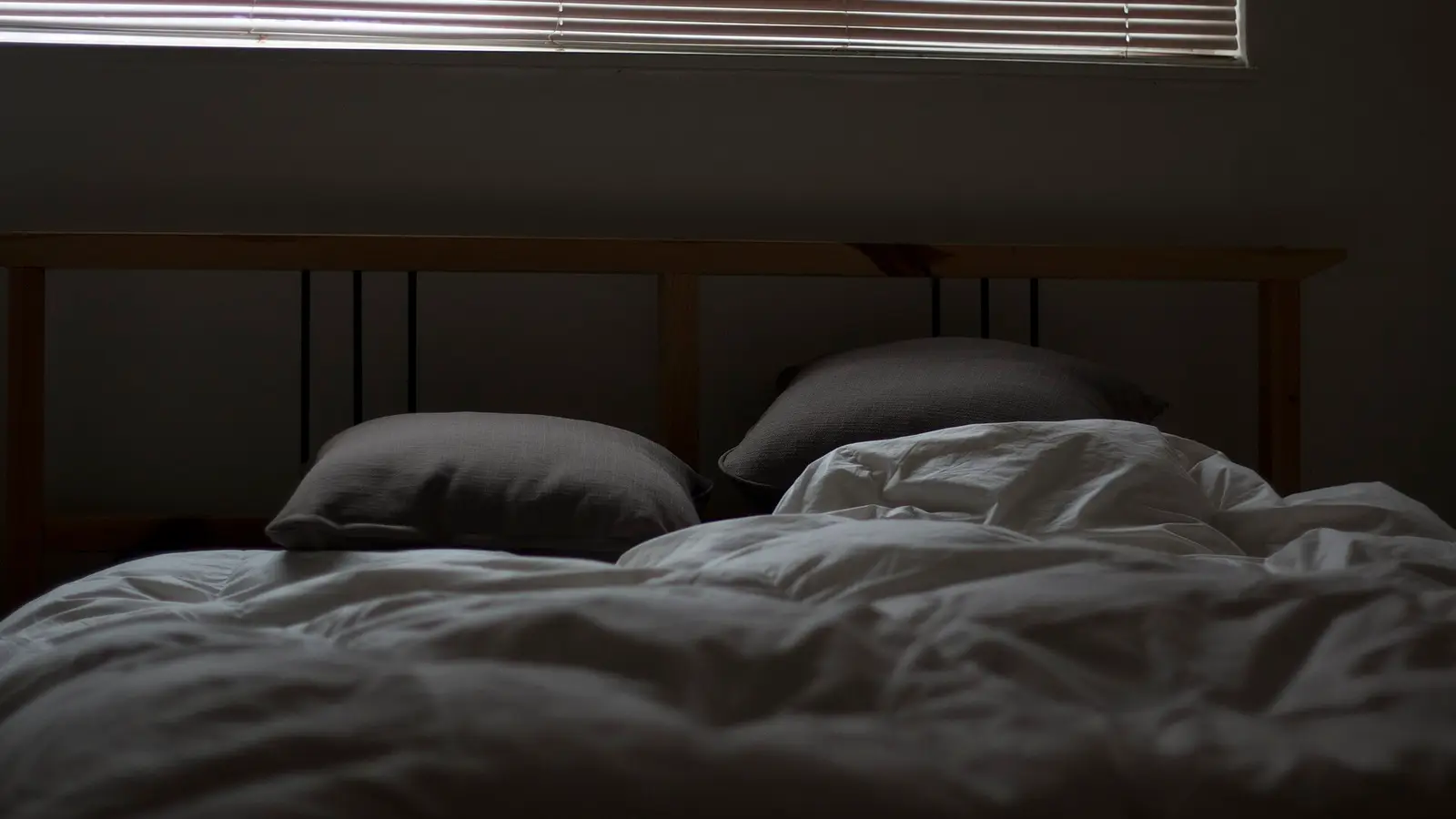 Lit défait aux draps gris, stores fermés