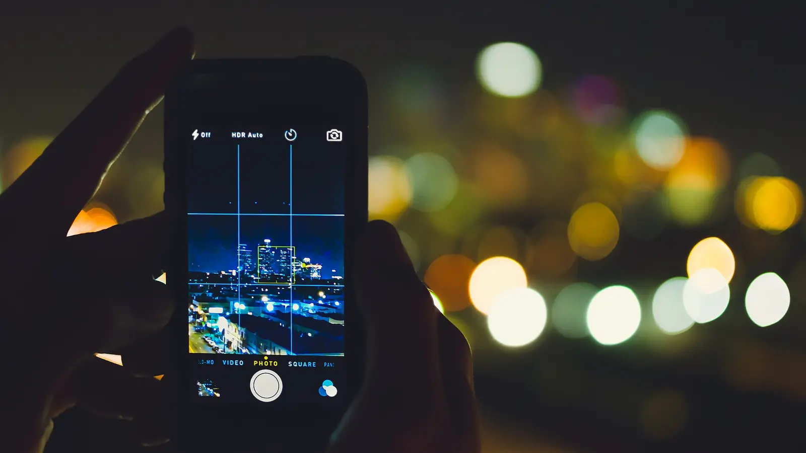 Main tenant un téléphone allumé devant les lumières floues d'une ville la nuit